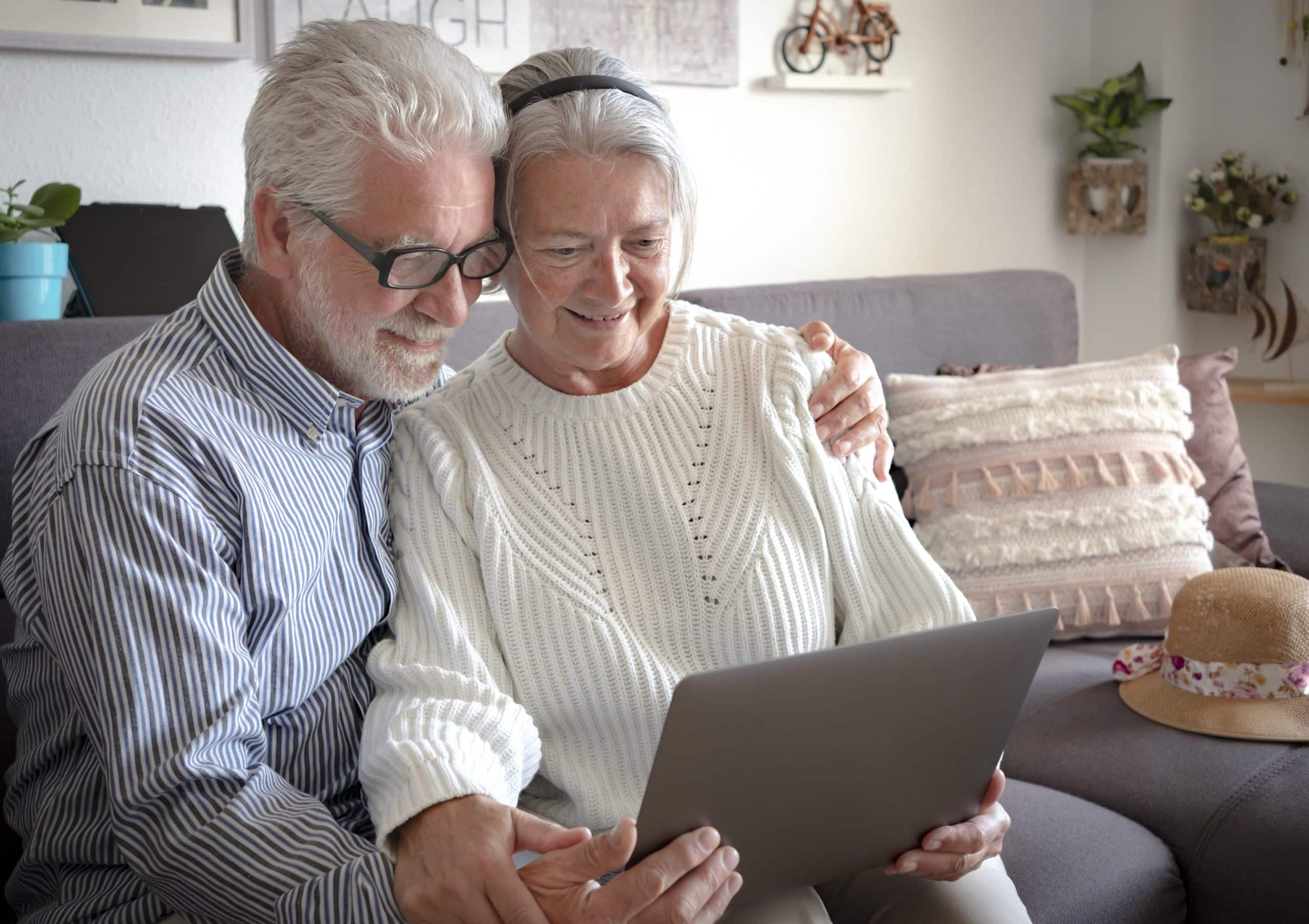 Elderly web surfer. Two smiling senior people sharing and looking at laptop and planning a new travel. White hair - couple in retirement